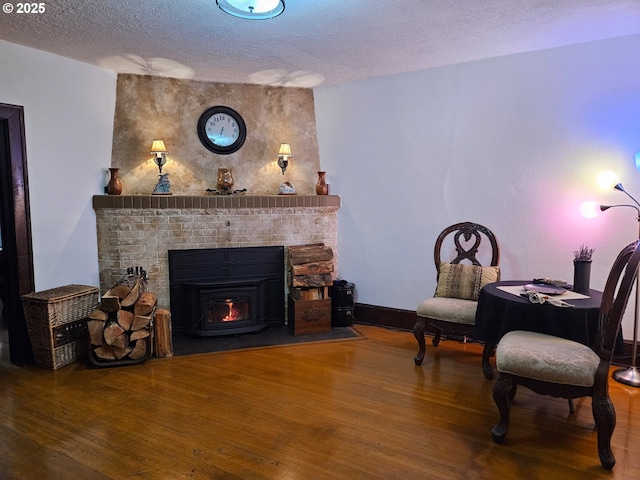 living area with a textured ceiling, a fireplace, wood finished floors, and baseboards