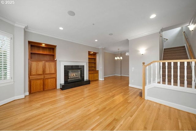 unfurnished living room featuring built in shelves, light hardwood / wood-style floors, a notable chandelier, and ornamental molding