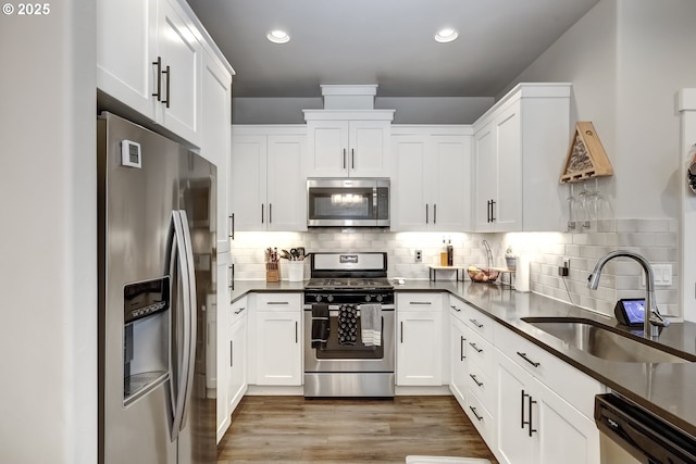 kitchen with stainless steel appliances, a sink, white cabinets, dark countertops, and recessed lighting