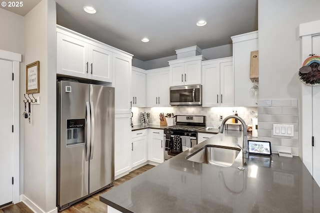 kitchen with appliances with stainless steel finishes, a sink, dark countertops, white cabinetry, and recessed lighting
