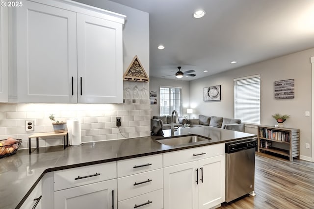 kitchen featuring dishwasher, a sink, dark countertops, open floor plan, and a ceiling fan