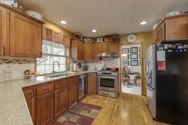 kitchen featuring light wood-style floors, appliances with stainless steel finishes, brown cabinets, under cabinet range hood, and a sink