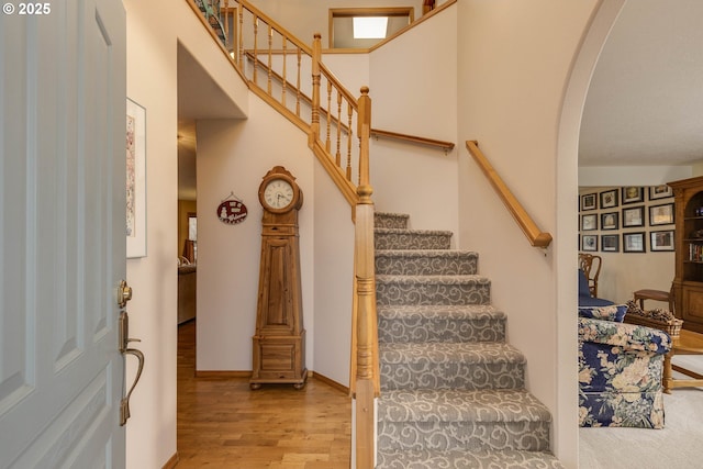 staircase featuring a towering ceiling, baseboards, arched walkways, and wood finished floors