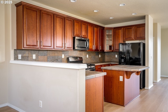 kitchen with glass insert cabinets, light wood finished floors, tasteful backsplash, and appliances with stainless steel finishes