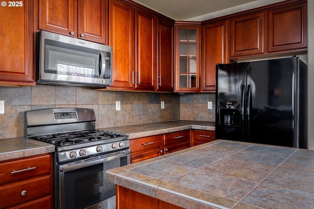 kitchen with stainless steel appliances, tasteful backsplash, brown cabinetry, and glass insert cabinets