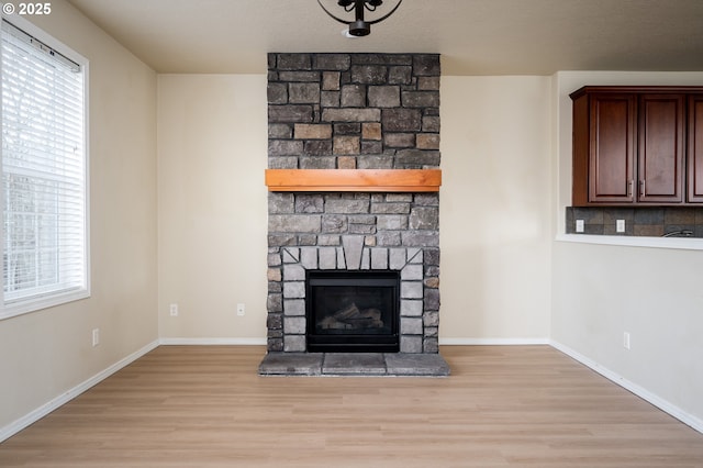 unfurnished living room featuring a stone fireplace, plenty of natural light, wood finished floors, and baseboards