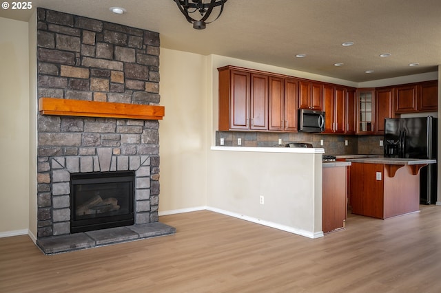 kitchen with black refrigerator with ice dispenser, stainless steel microwave, a kitchen bar, and light wood-style floors