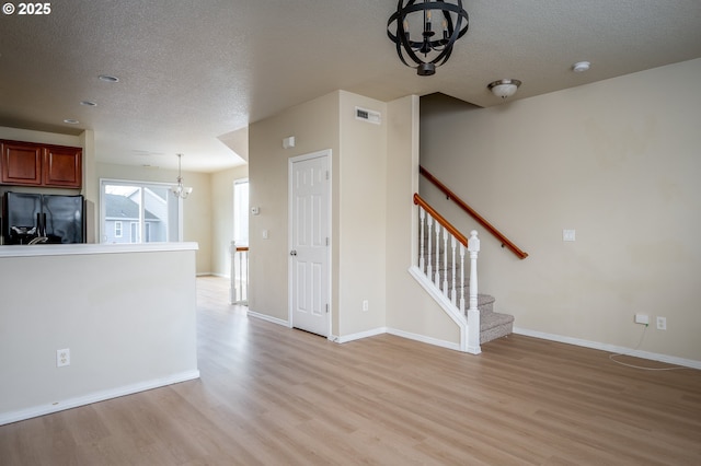 unfurnished living room with a chandelier, a textured ceiling, visible vents, stairs, and light wood finished floors