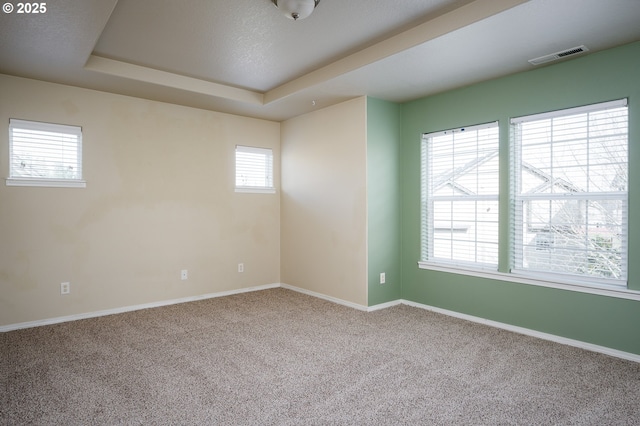 carpeted empty room with a tray ceiling, visible vents, and baseboards