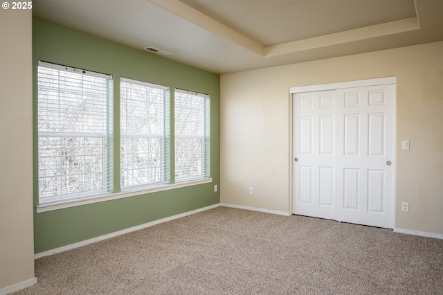 unfurnished bedroom featuring a tray ceiling, carpet, a closet, visible vents, and baseboards