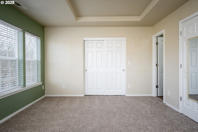 unfurnished bedroom with carpet floors, baseboards, and a raised ceiling