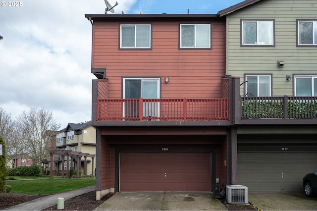 rear view of property with concrete driveway, central AC, a balcony, and an attached garage