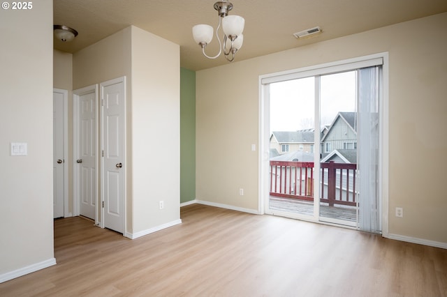 empty room featuring baseboards, a notable chandelier, visible vents, and wood finished floors