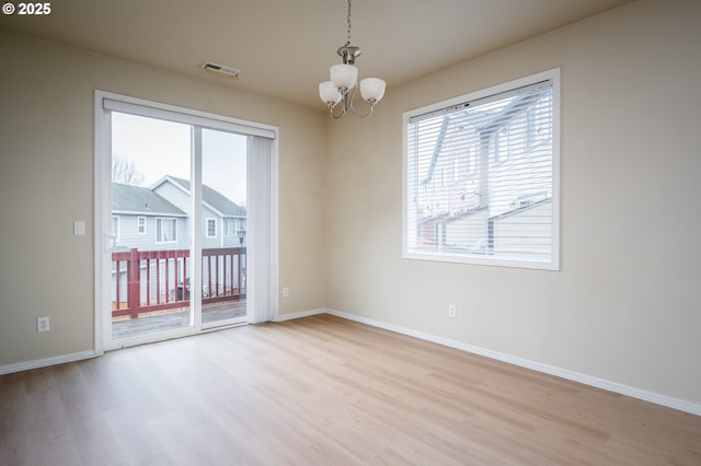 spare room featuring a notable chandelier, baseboards, a wealth of natural light, and wood finished floors