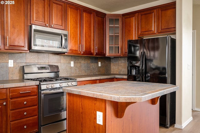 kitchen with stainless steel appliances, a kitchen island, a kitchen breakfast bar, tasteful backsplash, and glass insert cabinets