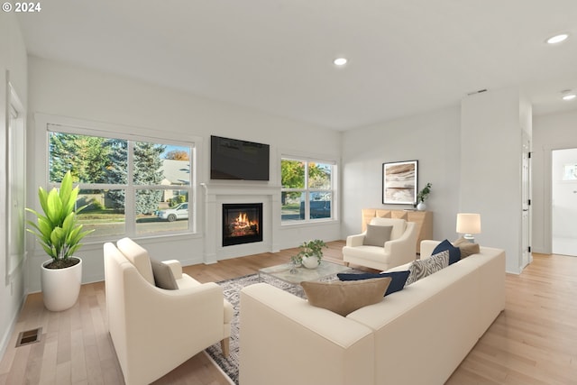 living area featuring recessed lighting, visible vents, a glass covered fireplace, and light wood-style flooring