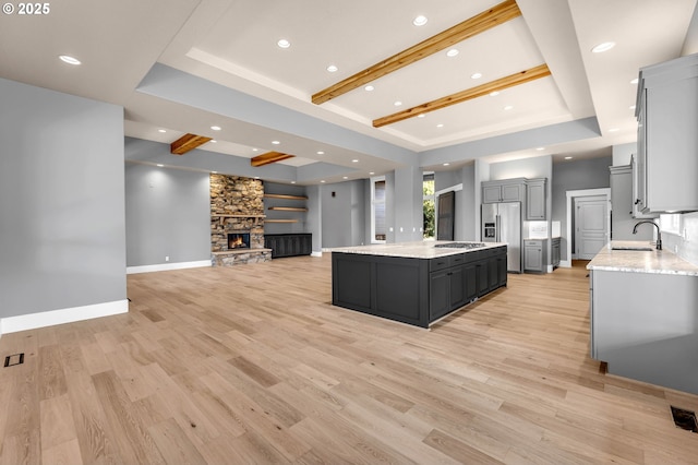 kitchen with a sink, a kitchen island, gray cabinets, a tray ceiling, and stainless steel fridge