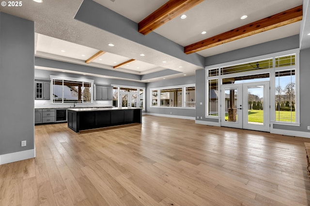 unfurnished living room with beverage cooler, baseboards, beamed ceiling, french doors, and light wood-style floors