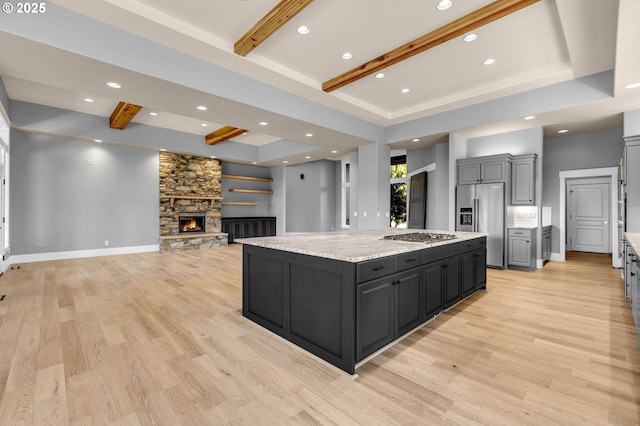 kitchen featuring light wood finished floors, a kitchen island, appliances with stainless steel finishes, and a stone fireplace