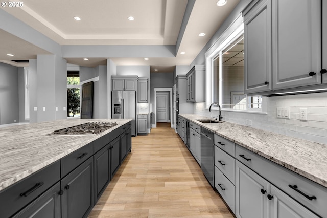 kitchen featuring tasteful backsplash, light stone countertops, gray cabinets, stainless steel appliances, and a sink