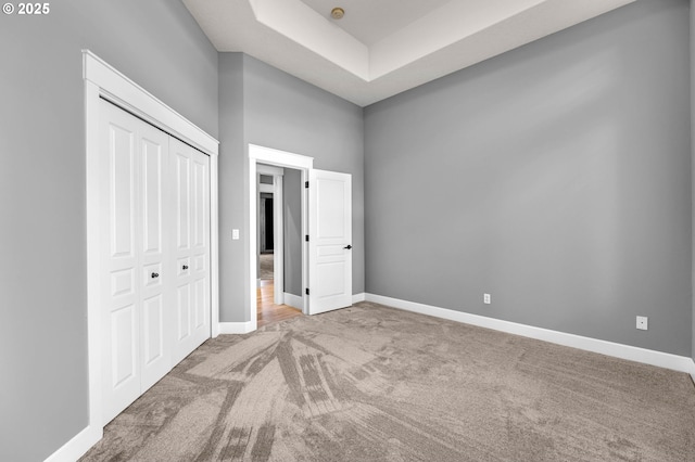 unfurnished bedroom featuring carpet floors, a closet, a high ceiling, and baseboards