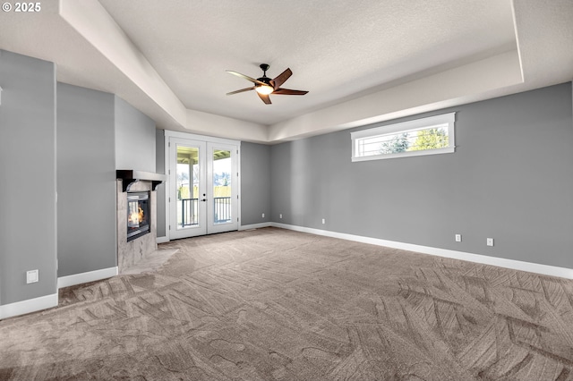 unfurnished living room featuring a tray ceiling, french doors, carpet flooring, and baseboards