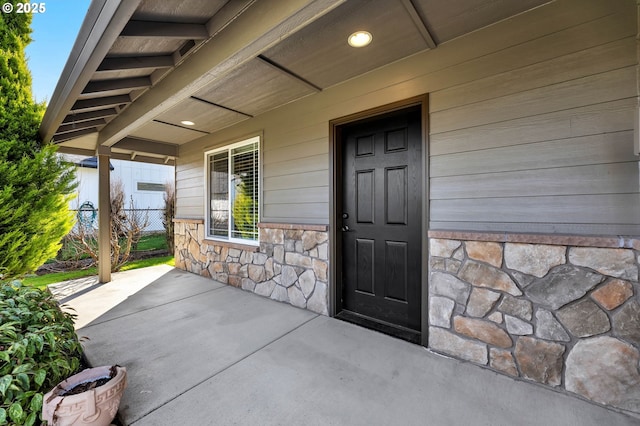 view of exterior entry with stone siding, a patio area, and fence