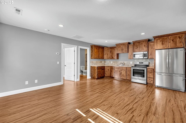 kitchen featuring appliances with stainless steel finishes, brown cabinets, visible vents, and light wood-style flooring