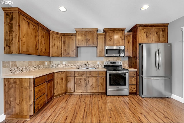 kitchen featuring stainless steel appliances, light wood finished floors, a sink, and light countertops