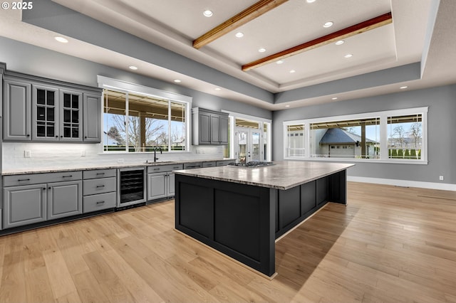 kitchen with a raised ceiling, wine cooler, gray cabinetry, light wood-style floors, and a sink