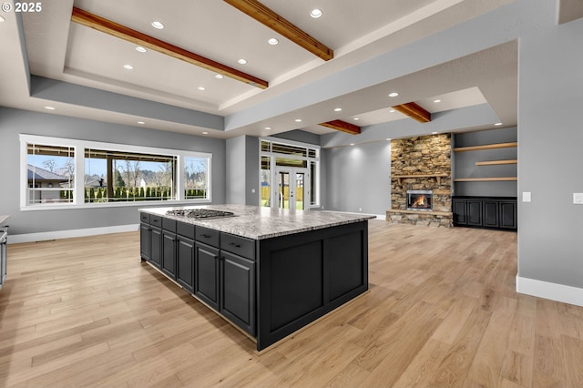 kitchen with a fireplace, a kitchen island, baseboards, light wood-style floors, and dark cabinetry