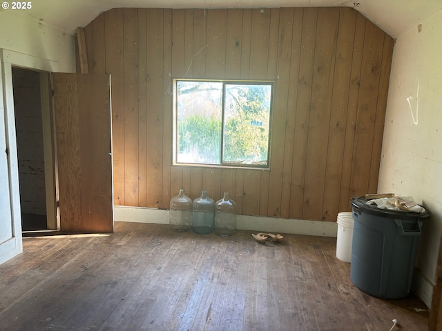 unfurnished room featuring hardwood / wood-style floors, wood walls, and vaulted ceiling