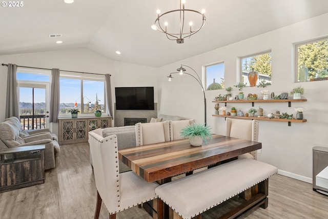 dining space featuring plenty of natural light, vaulted ceiling, light wood-style floors, and a notable chandelier