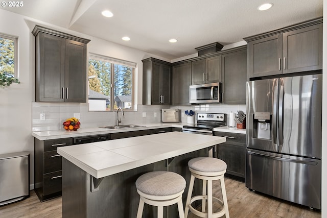 kitchen featuring light wood-style flooring, a sink, backsplash, a kitchen island, and appliances with stainless steel finishes