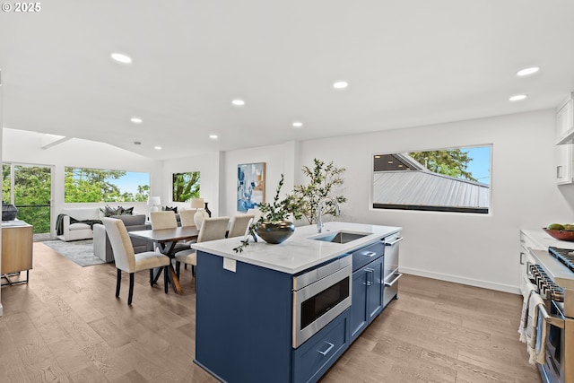kitchen with stainless steel appliances, blue cabinets, a sink, light wood-style flooring, and recessed lighting