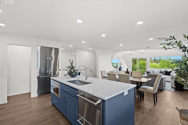 kitchen featuring stainless steel appliances, blue cabinets, a sink, wood finished floors, and recessed lighting