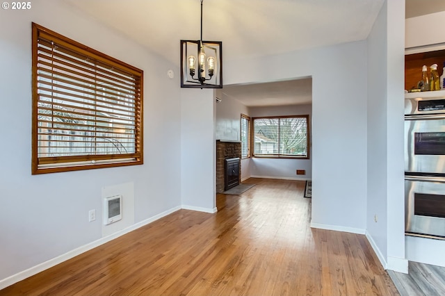 unfurnished living room featuring visible vents, a fireplace with flush hearth, a notable chandelier, wood finished floors, and baseboards