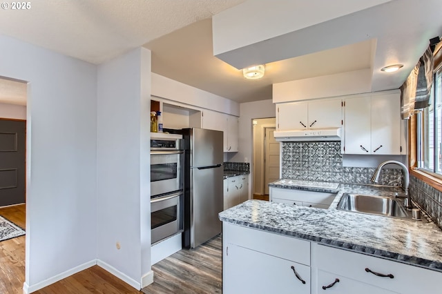 kitchen featuring wood finished floors, a sink, appliances with stainless steel finishes, under cabinet range hood, and white cabinetry