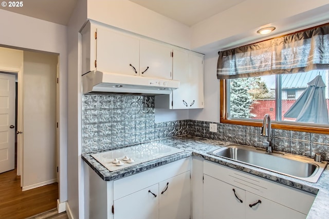 kitchen with under cabinet range hood, white electric cooktop, wood finished floors, white cabinetry, and a sink