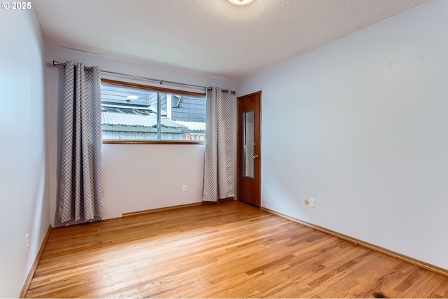 empty room featuring light wood-style flooring, baseboards, and a textured ceiling