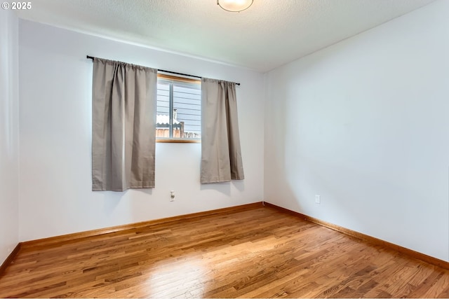 empty room with a textured ceiling, baseboards, and wood finished floors