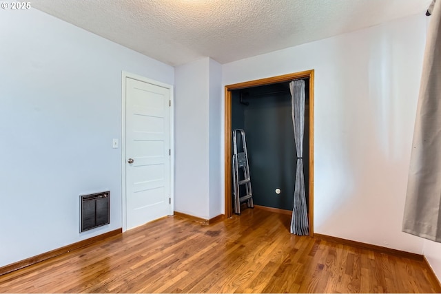 unfurnished bedroom featuring heating unit, baseboards, light wood-type flooring, and a textured ceiling