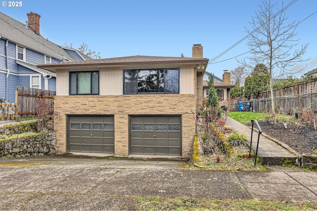 exterior space with a garage, concrete driveway, a chimney, and fence