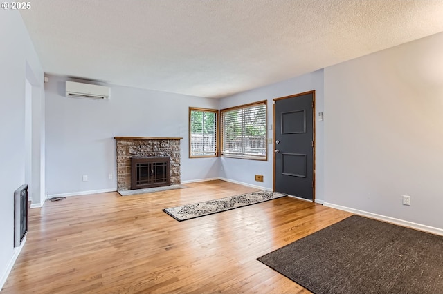 unfurnished living room with wood finished floors, baseboards, a stone fireplace, a wall mounted air conditioner, and a textured ceiling