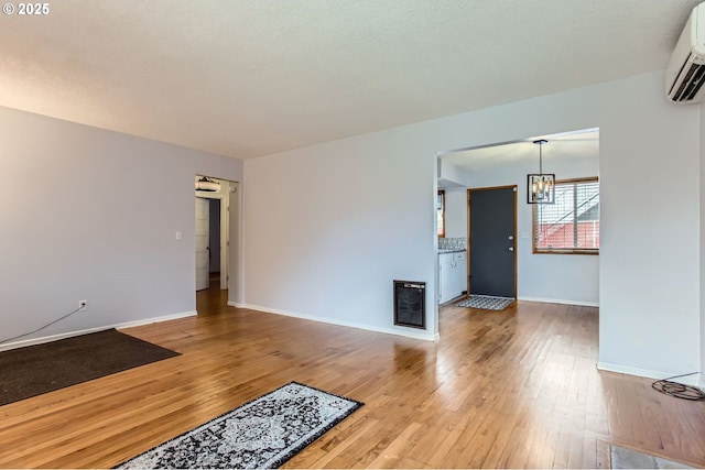 unfurnished living room featuring a wall mounted AC, a textured ceiling, light wood-style floors, baseboards, and a chandelier