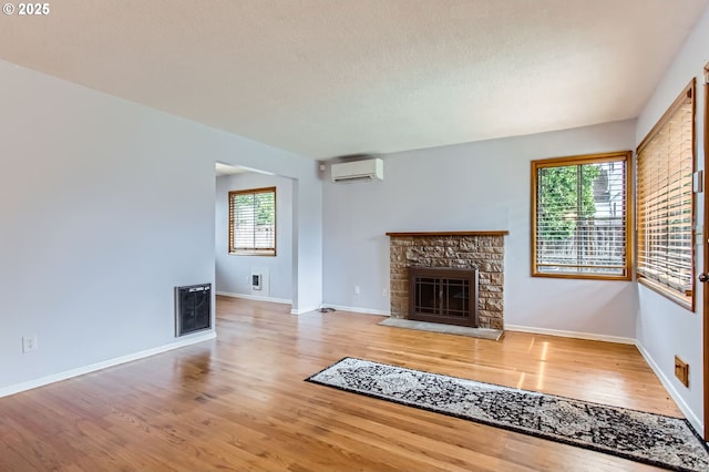 unfurnished living room featuring an AC wall unit, plenty of natural light, a stone fireplace, and wood finished floors