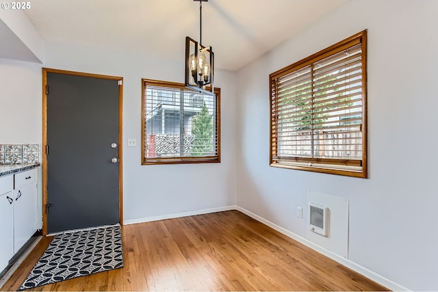 unfurnished dining area featuring heating unit, baseboards, a notable chandelier, and light wood-style flooring