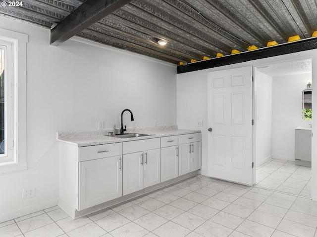 kitchen with white cabinetry, light stone countertops, and sink