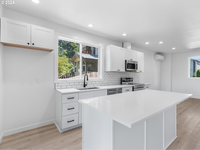 kitchen with sink, stainless steel appliances, a center island, white cabinets, and an AC wall unit