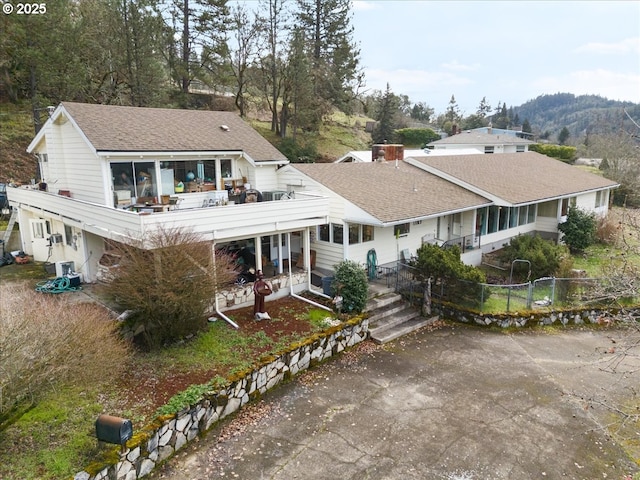 back of house featuring a sunroom, a shingled roof, fence, and concrete driveway